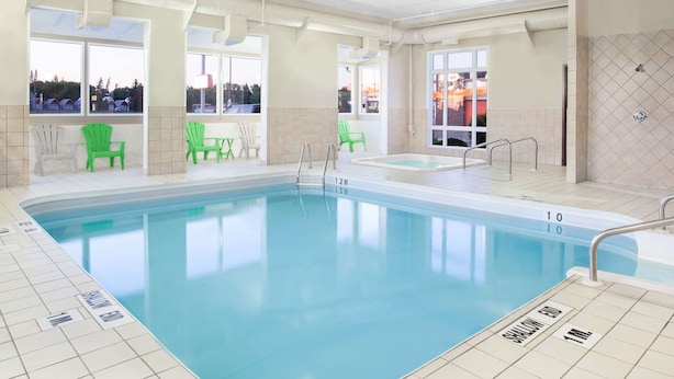 Una piscina interior con agua cristalina, zonas de profundidad señalizadas y sillas verdes alrededor del borde.