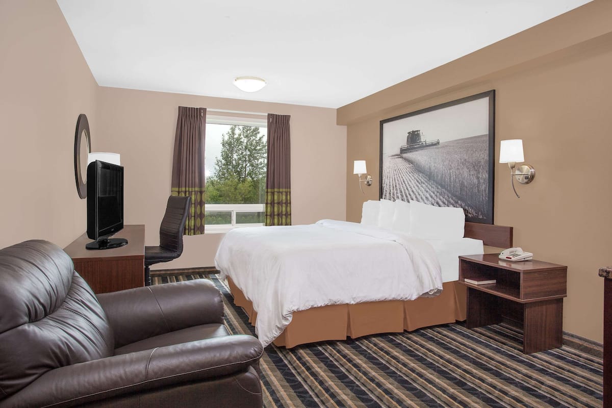 A hotel room with a large bed, a leather sofa, a television, and a painting on the wall.
