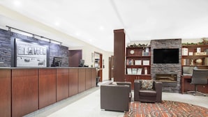 Un área de recepción con pared de piedra, televisor de pantalla plana, chimenea y zona de estar con alfombra estampada.