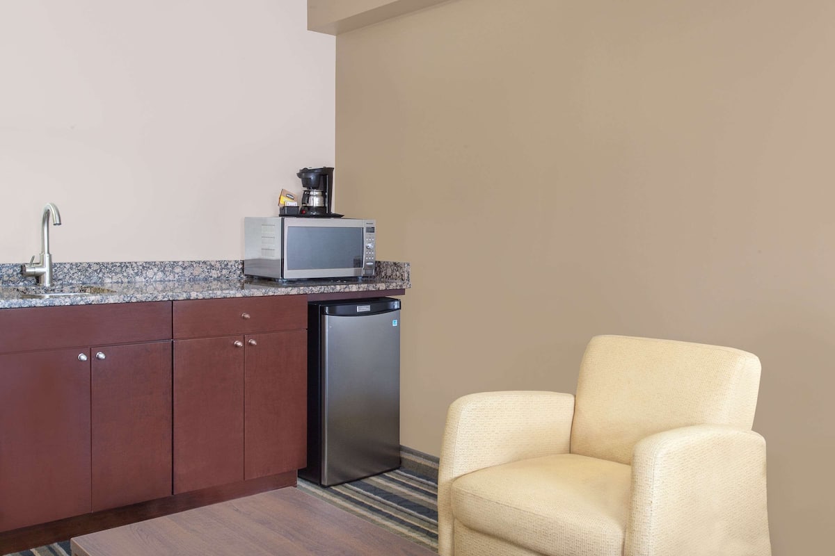 A compact kitchen with a microwave, coffee maker, and dishwasher. A beige armchair is positioned near the kitchen.
