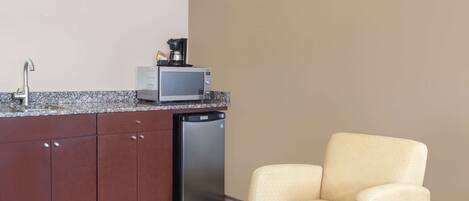 Cocina compacta con microondas, cafetera y lavavajillas. Un sillón color beige está ubicado cerca de la cocina.