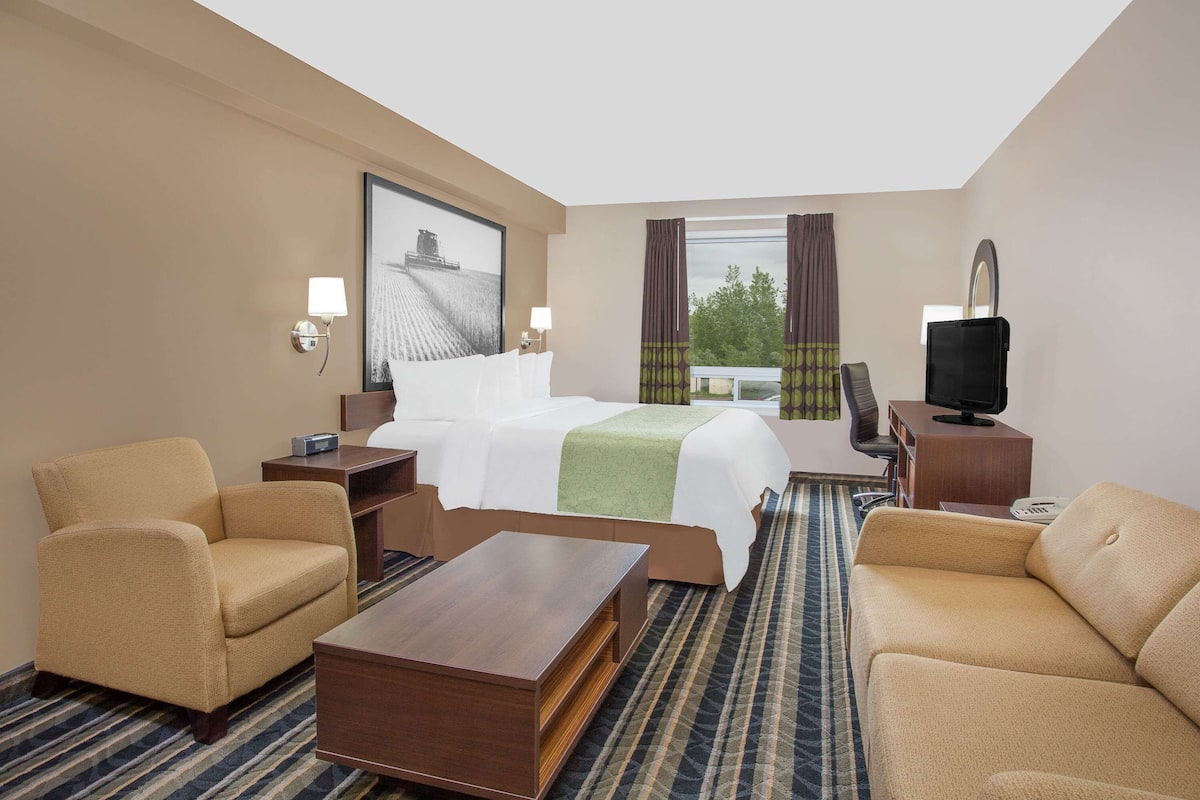 A hotel room with a bed, two armchairs, a coffee table, a TV, and a large window with curtains.