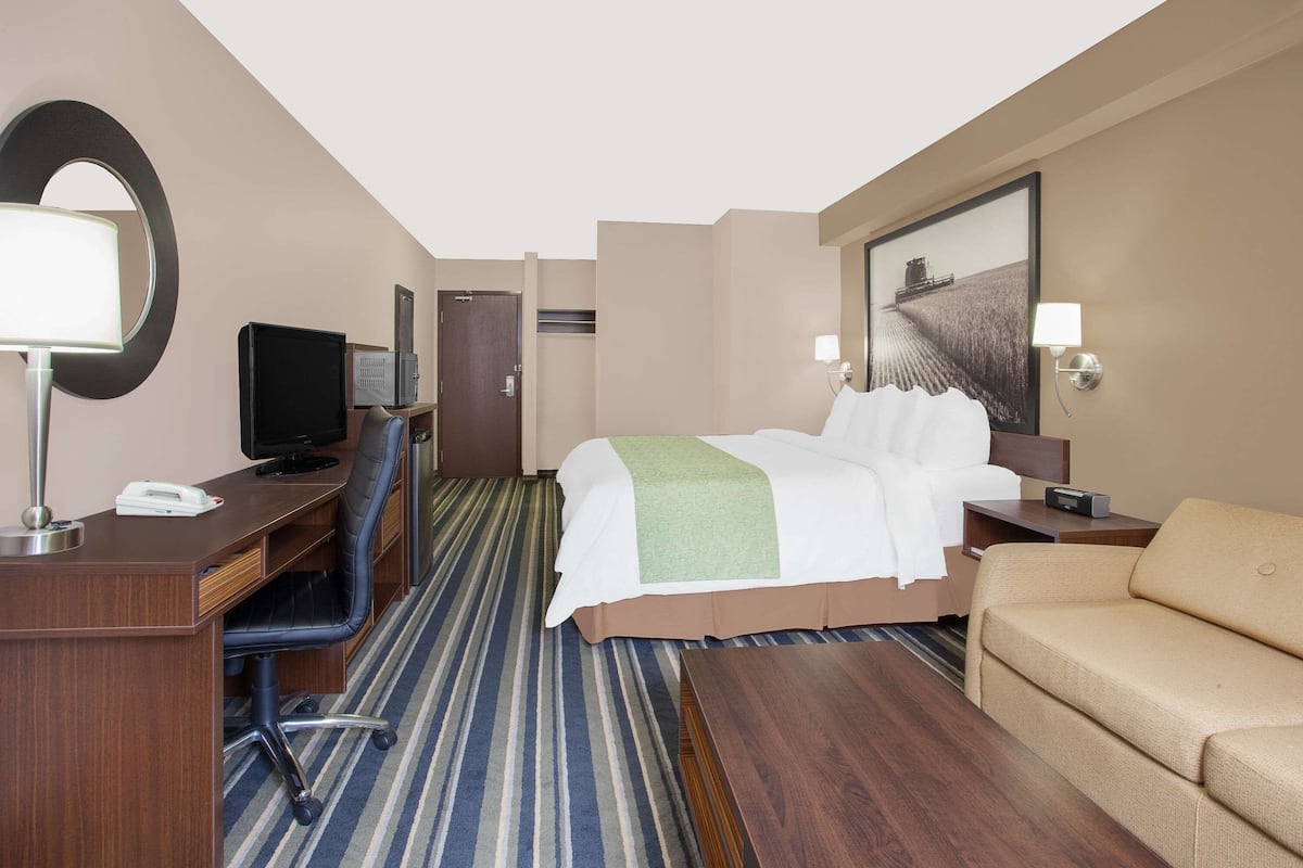 A hotel room with a bed, a desk with a computer, a chair, a sofa, and a large mirror.