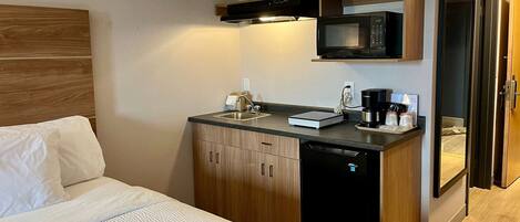 Habitación de hotel compacta con cama, una pequeña cocina equipada con microondas, cafetera y lavavajillas.