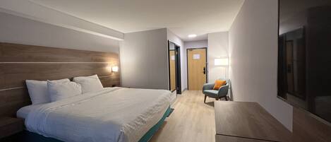 Ein Hotelzimmer mit einem großen Bett, einem Sessel, einem Fernseher und einer Tür.