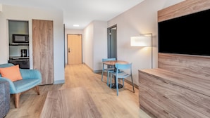 A modern hotel room with a wooden floor, a sofa, a dining table with chairs, a TV, and a microwave. - Super 8 by Wyndham Cornwall ON (Cornwall)