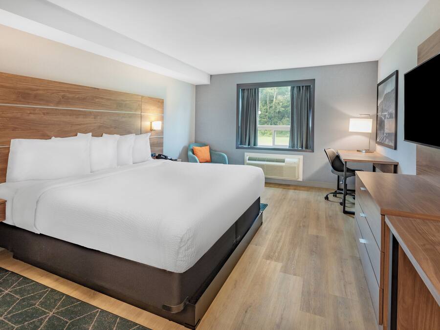 Una camera d'albergo moderna con un letto grande, una scrivania, una sedia, una televisione e una finestra con tende.