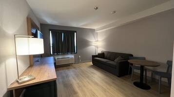A modern, well-lit room with a wooden desk, a grey sofa, a small round table, and a floor lamp.