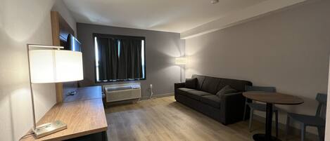 A modern, well-lit room with a wooden desk, a grey sofa, a small round table, and a floor lamp.
