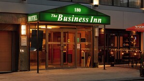 Entrada de un hotel con un toldo verde que muestra la leyenda “The Business Inn” y el número “180”.