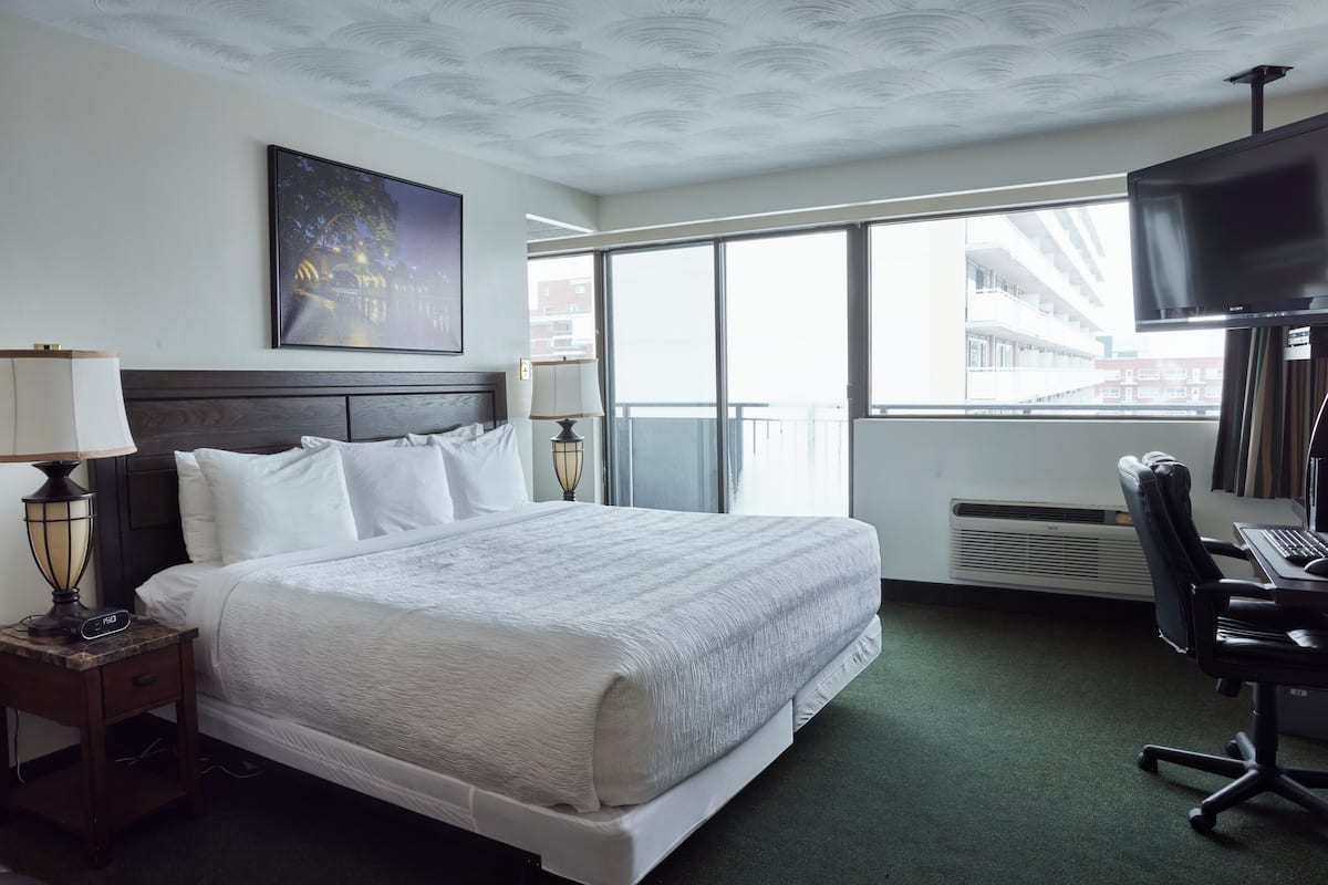 Quarto de hotel com uma cama grande, uma mesa com computador, televisão e janela com vista para edifícios.