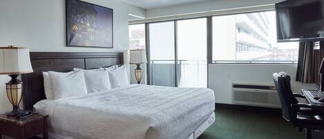 Habitación de hotel con una cama grande, un escritorio con computadora, un televisor y una ventana con vistas a edificios.