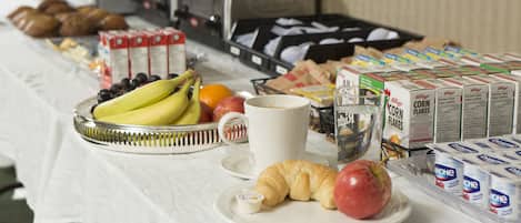 Et morgenbord med et udvalg af madvarer, herunder frugt, en croissant, en muffin og cornflakes.
