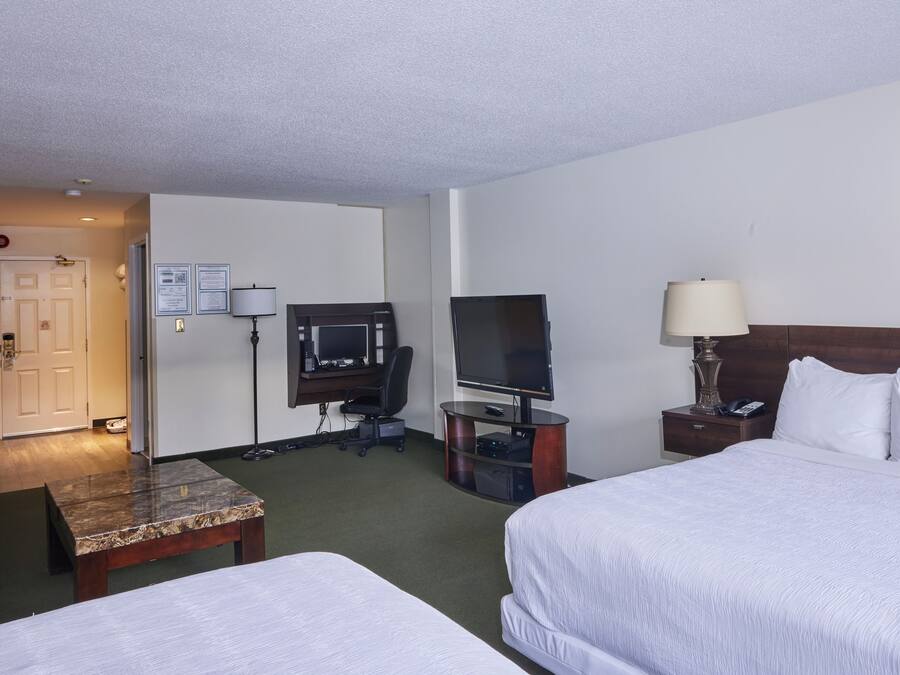 A hotel room with two beds, a desk with a computer, a TV, and a lamp.