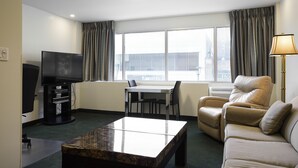 Habitación de hotel con televisión de pantalla plana, una mesa de comedor con sillas, un sofá y una lámpara.