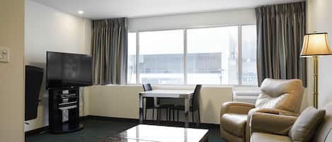 Habitación de hotel con televisión de pantalla plana, una mesa de comedor con sillas, un sofá y una lámpara.
