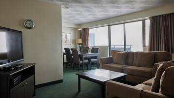 A hotel room with a television, sofa, coffee table, and a dining area with chairs and a table.