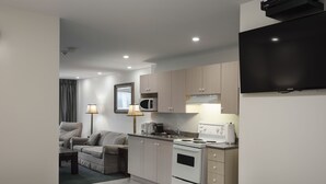 A compact kitchen with a microwave, stove, and sink, adjacent to a living area with a sofa and lamp.