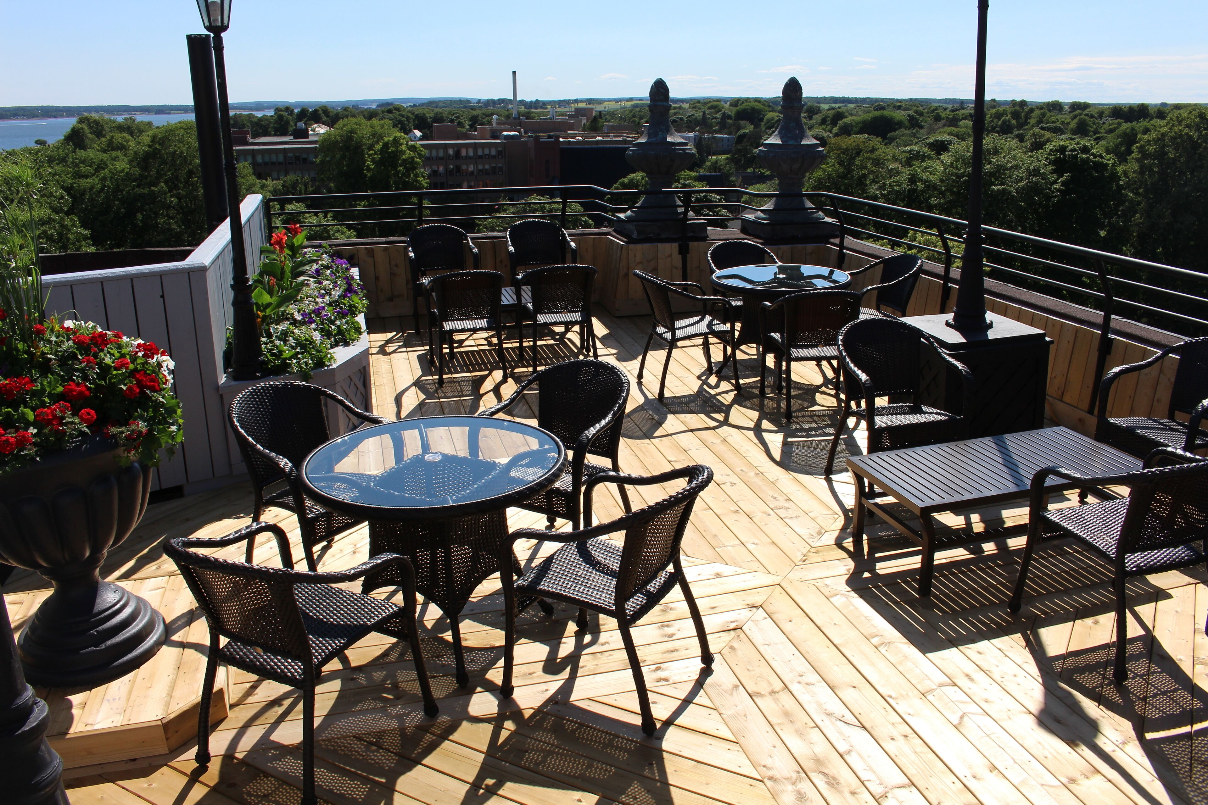 A wooden deck with outdoor furniture, including round tables and chairs, overlooking a scenic view of trees and a body of water.