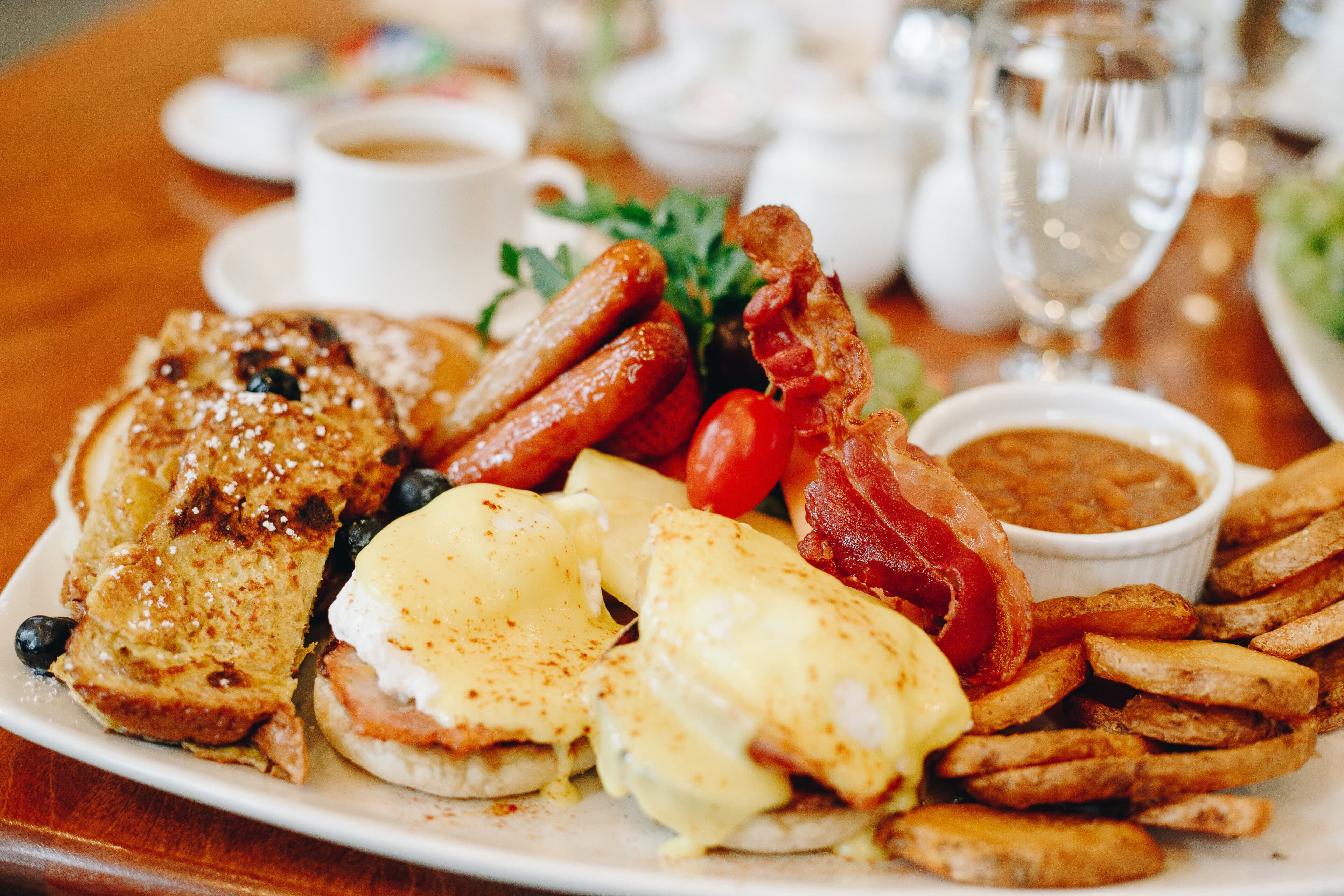 A breakfast plate with eggs, bacon, sausages, toast, and fries.