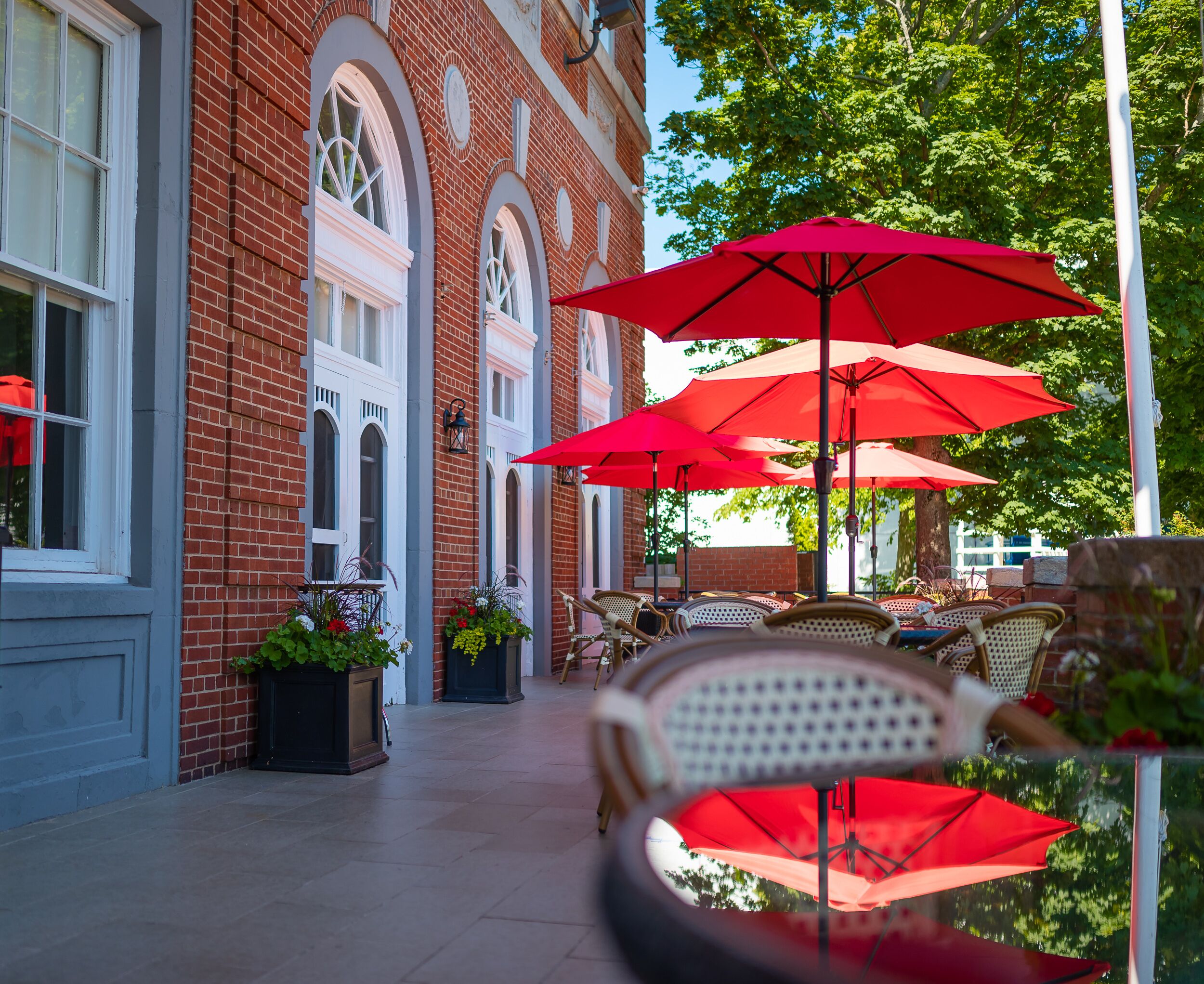 A brick building with arched windows and outdoor seating with red umbrellas.