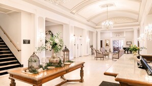 Un vestíbulo amplio con una imponente escalera, elegantes candelabros y un largo mostrador de recepción.