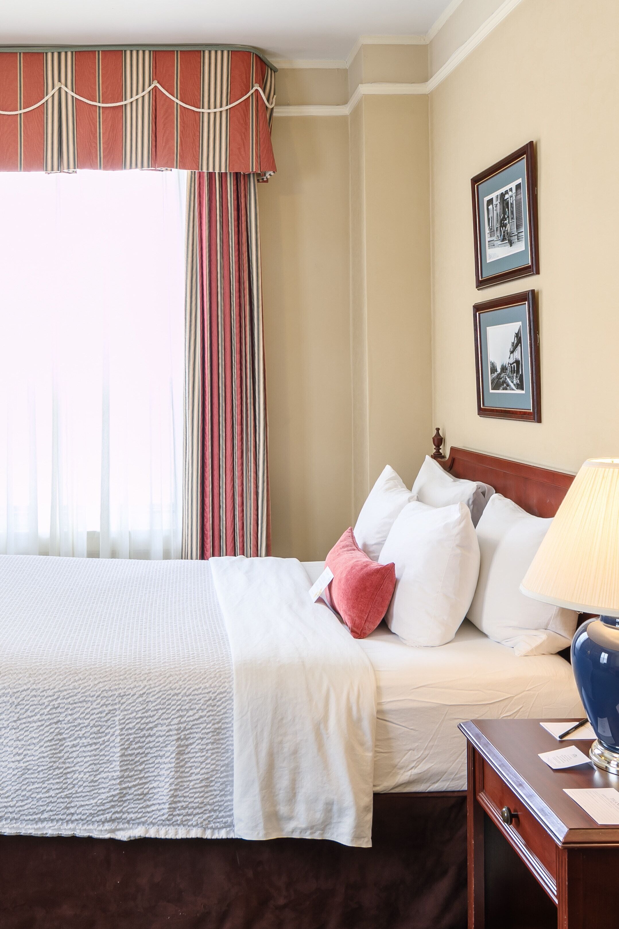 A hotel room with a large bed, striped curtains, a wooden headboard, and two framed pictures on the wall.