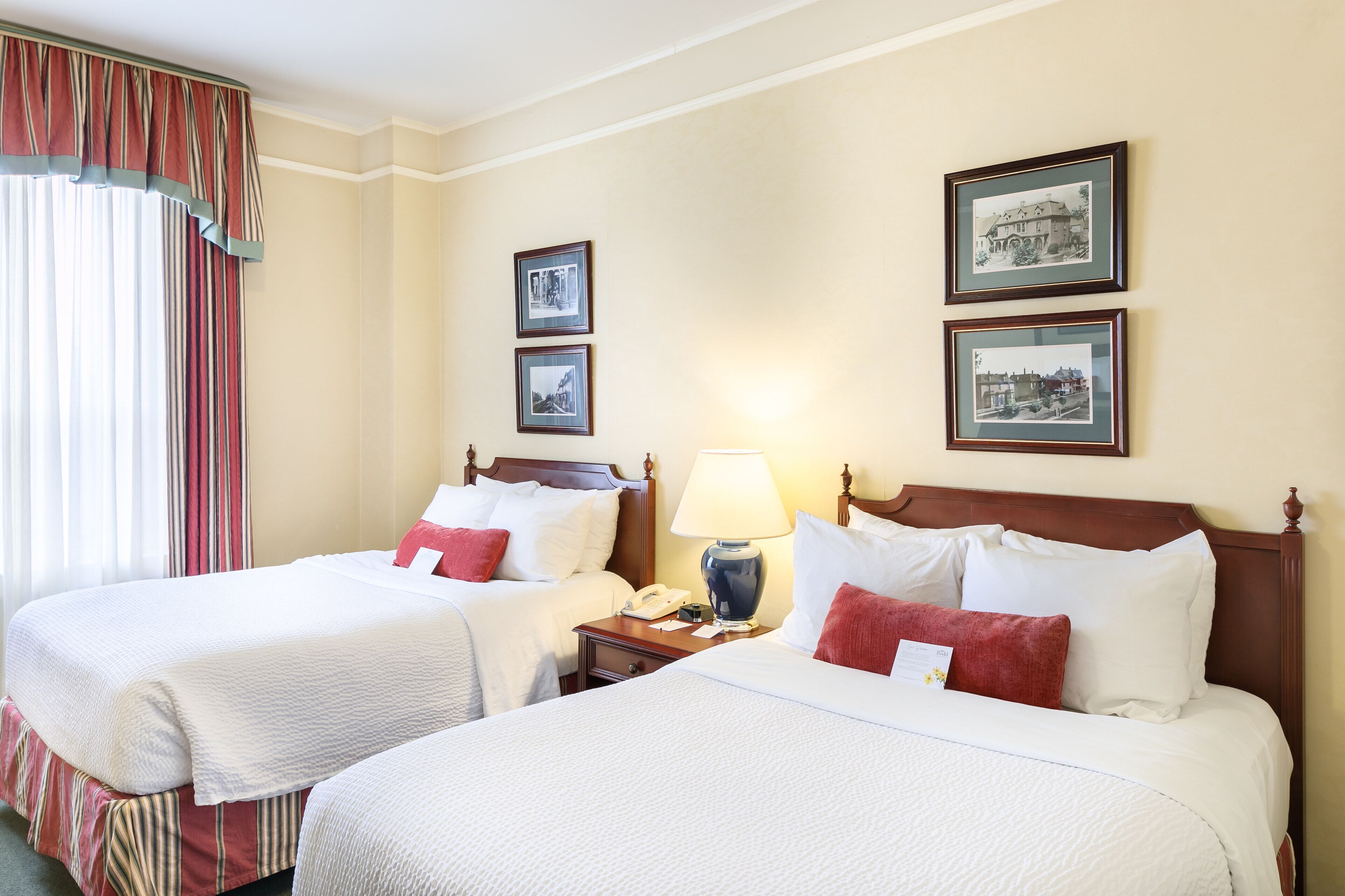 A hotel room with two beds, a nightstand with a lamp, and three framed pictures on the wall.