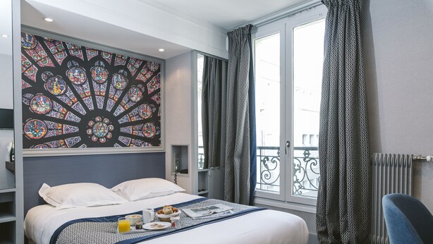 Una camera d'albergo con un letto grande, un vassoio per la colazione, una finestra decorativa in vetro colorato e un balcone con tende a motivi.