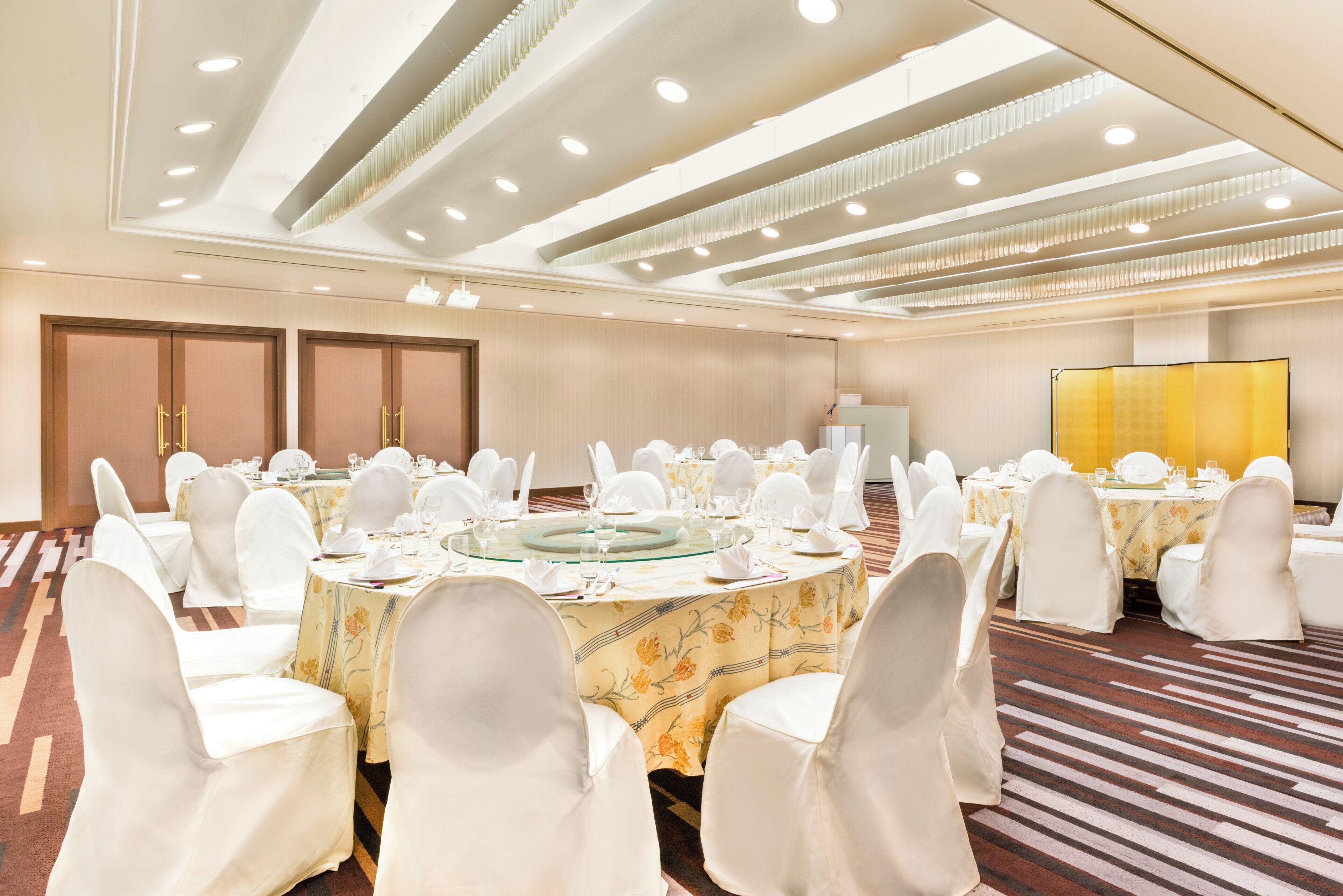 A banquet hall with round tables set for dining, white chairs, and a stage with a screen.