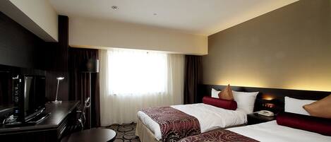 A hotel room with two beds, a desk with a computer, a TV, and a lamp.