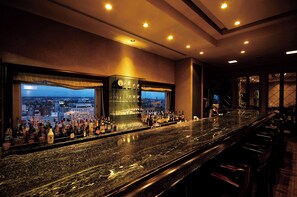 Un bar con vista a la ciudad, botellas de licores y un expositor de vidrio.