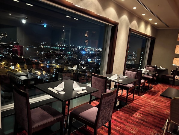 A restaurant with tables and chairs, large windows with a city view, and a red carpeted floor. - Crowne Plaza ANA Kushiro by IHG (Kushiro)