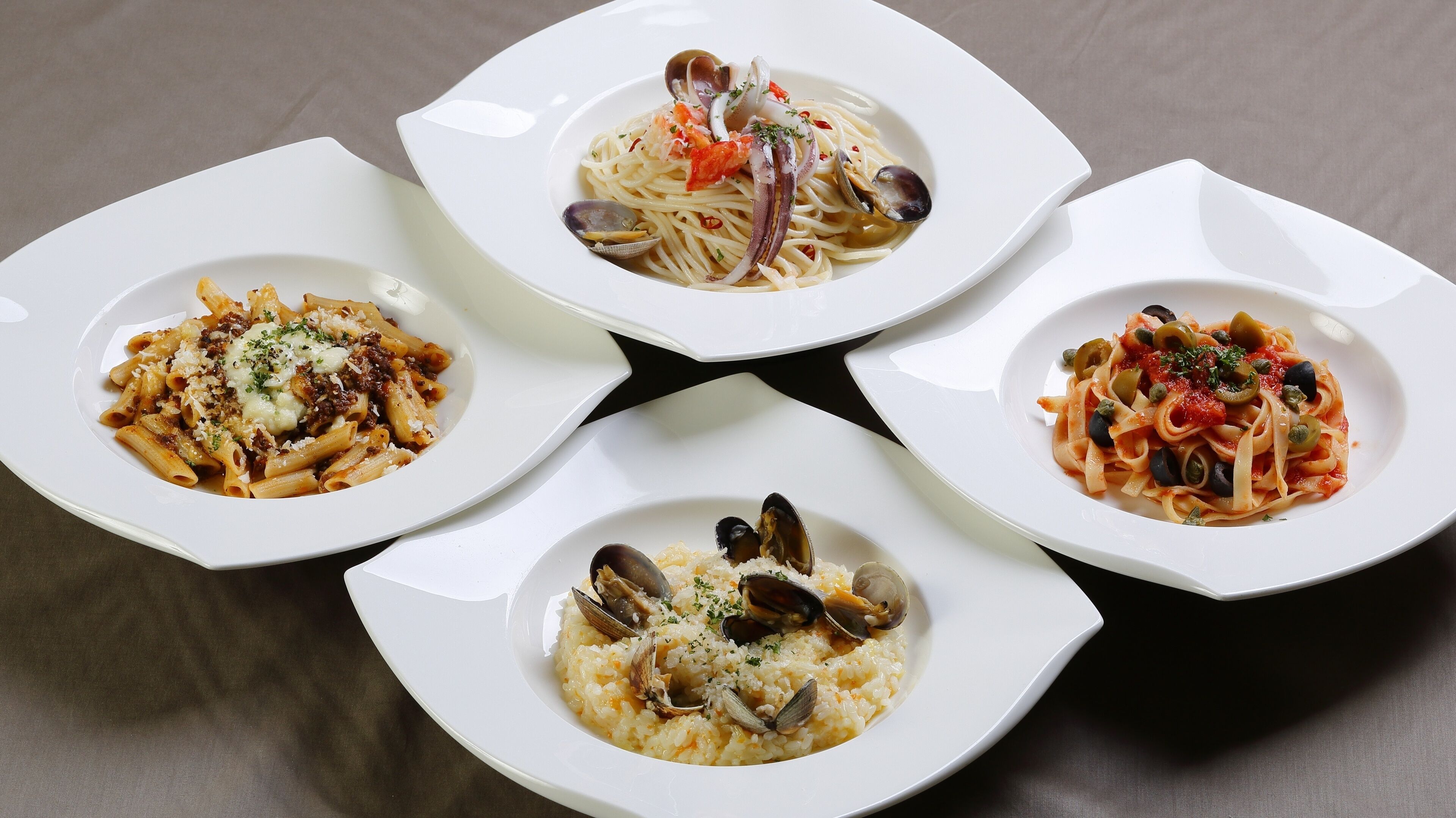Four white plates of pasta dishes with seafood, arranged on a table.