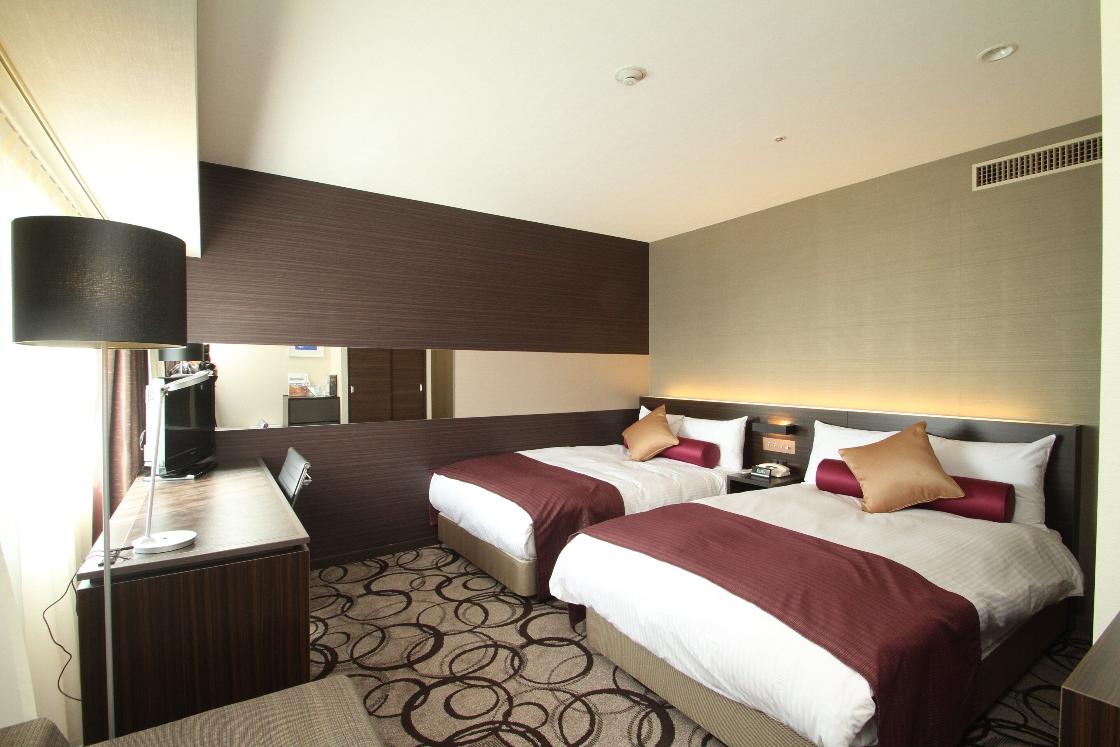 Une chambre d’hôtel avec deux lits, un bureau, une lampe et un miroir.