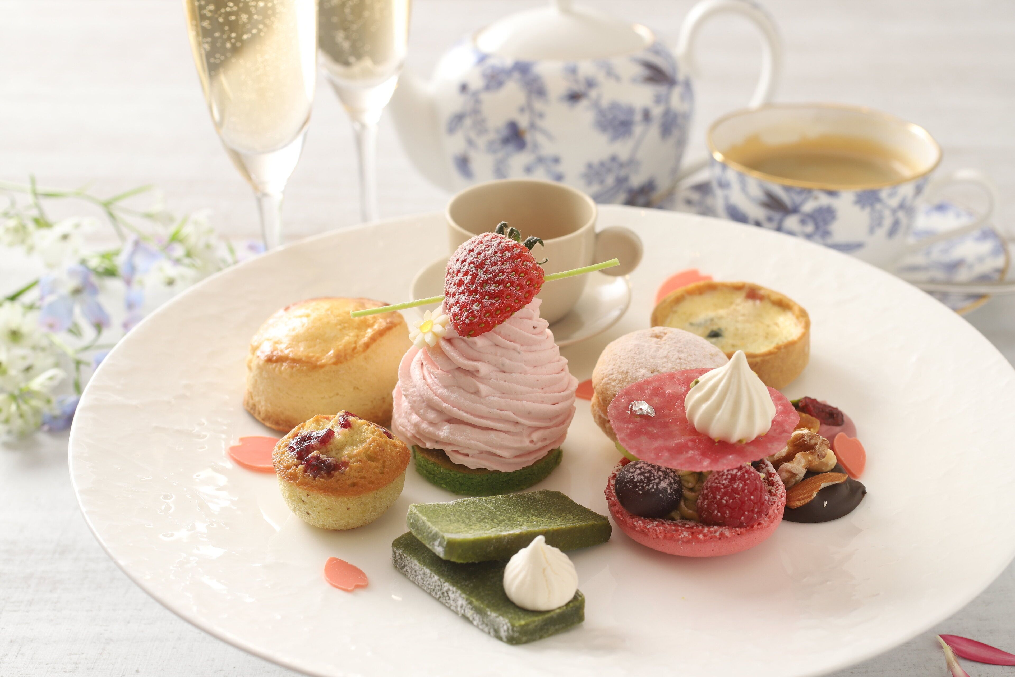 A variety of pastries and desserts on a plate, accompanied by a teapot and cups, suggesting a tea service setting.