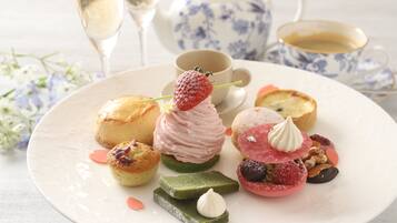 A variety of pastries and desserts on a plate, accompanied by a teapot and cups, suggesting a tea service setting.