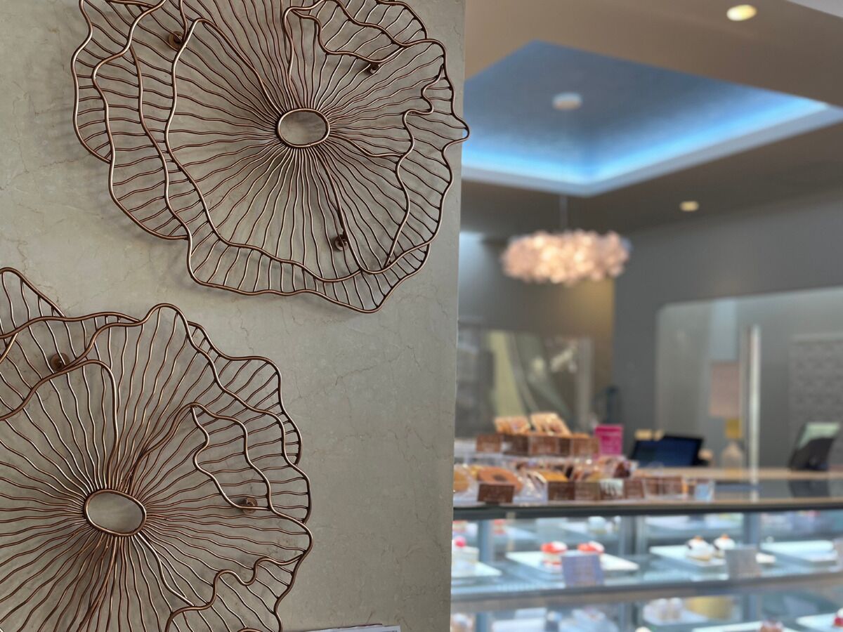 Una pared con un diseño floral de metal y una vitrina de panadería con diversos productos horneados.