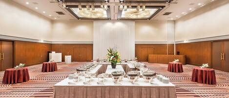 Un amplio salón de banquetes con una larga mesa dispuesta para un evento formal, rodeado de paneles de madera y grandes candelabros.