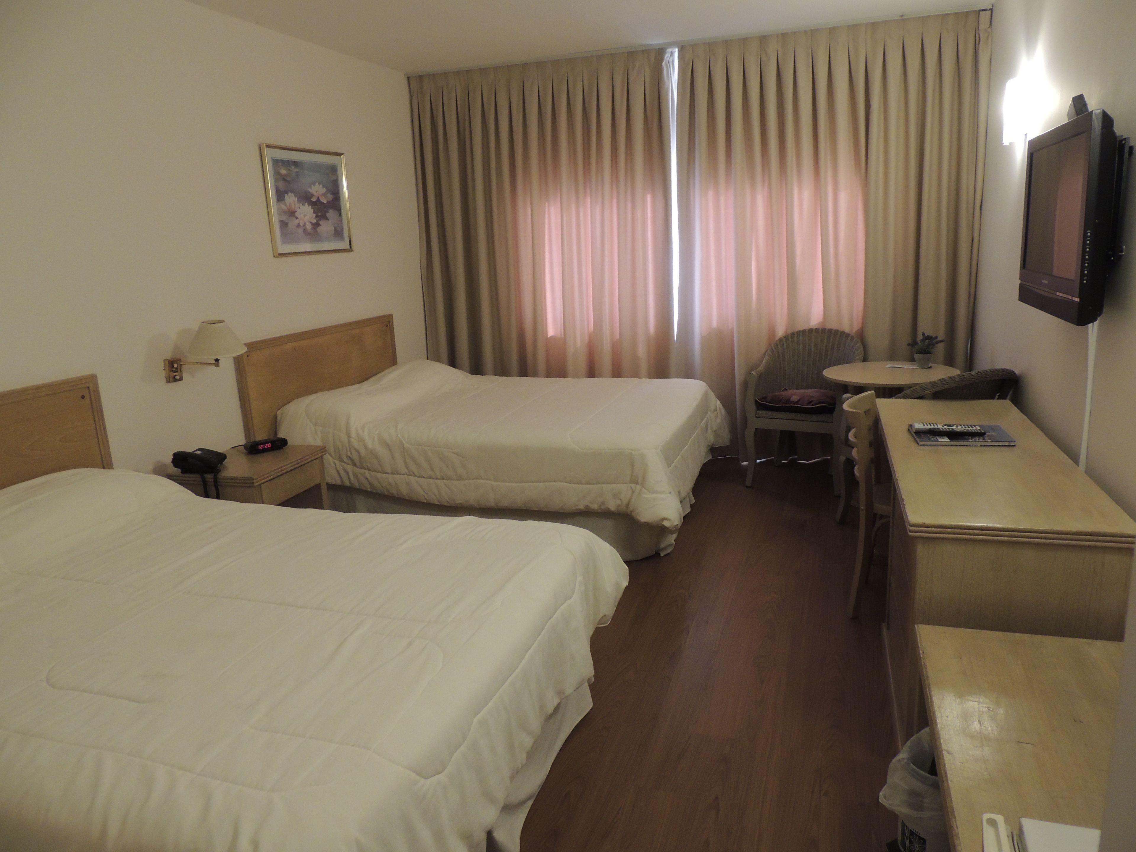 Habitación de hotel con dos camas, un escritorio, una silla, una lámpara, un televisor y una ventana con cortinas.