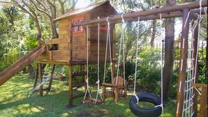 Une structure de jeu en bois comprenant un toboggan, des balançoires et une balançoire en forme de pneu.