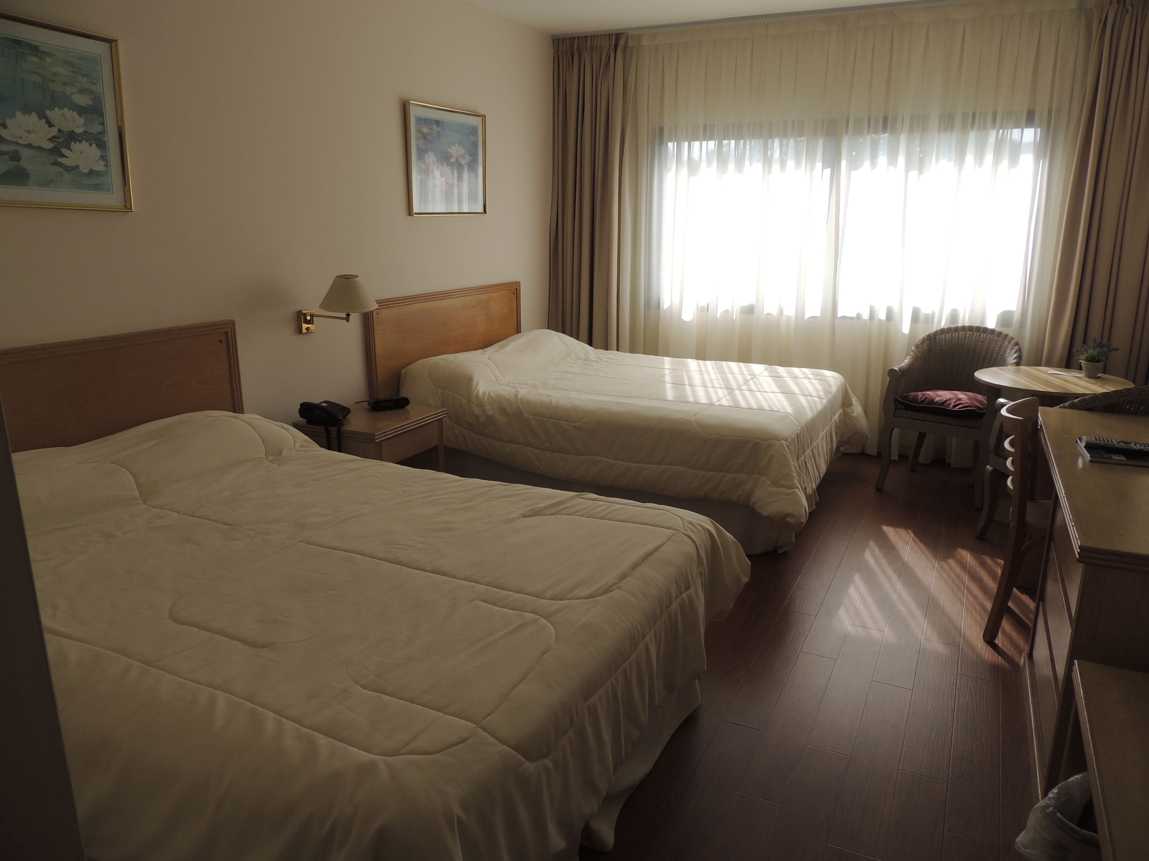 Una habitación de hotel con dos camas, un escritorio con una silla, una lámpara y una ventana con cortinas.