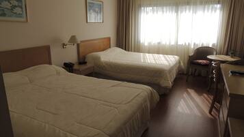 Una habitación de hotel con dos camas, un escritorio con una silla, una lámpara y una ventana con cortinas.