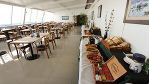 Un vaste espace dédié à la restauration, avec de nombreuses tables et chaises, un long comptoir où sont disposés des paniers et des produits alimentaires, et une vue sur la mer grâce à de grandes fenêtres.