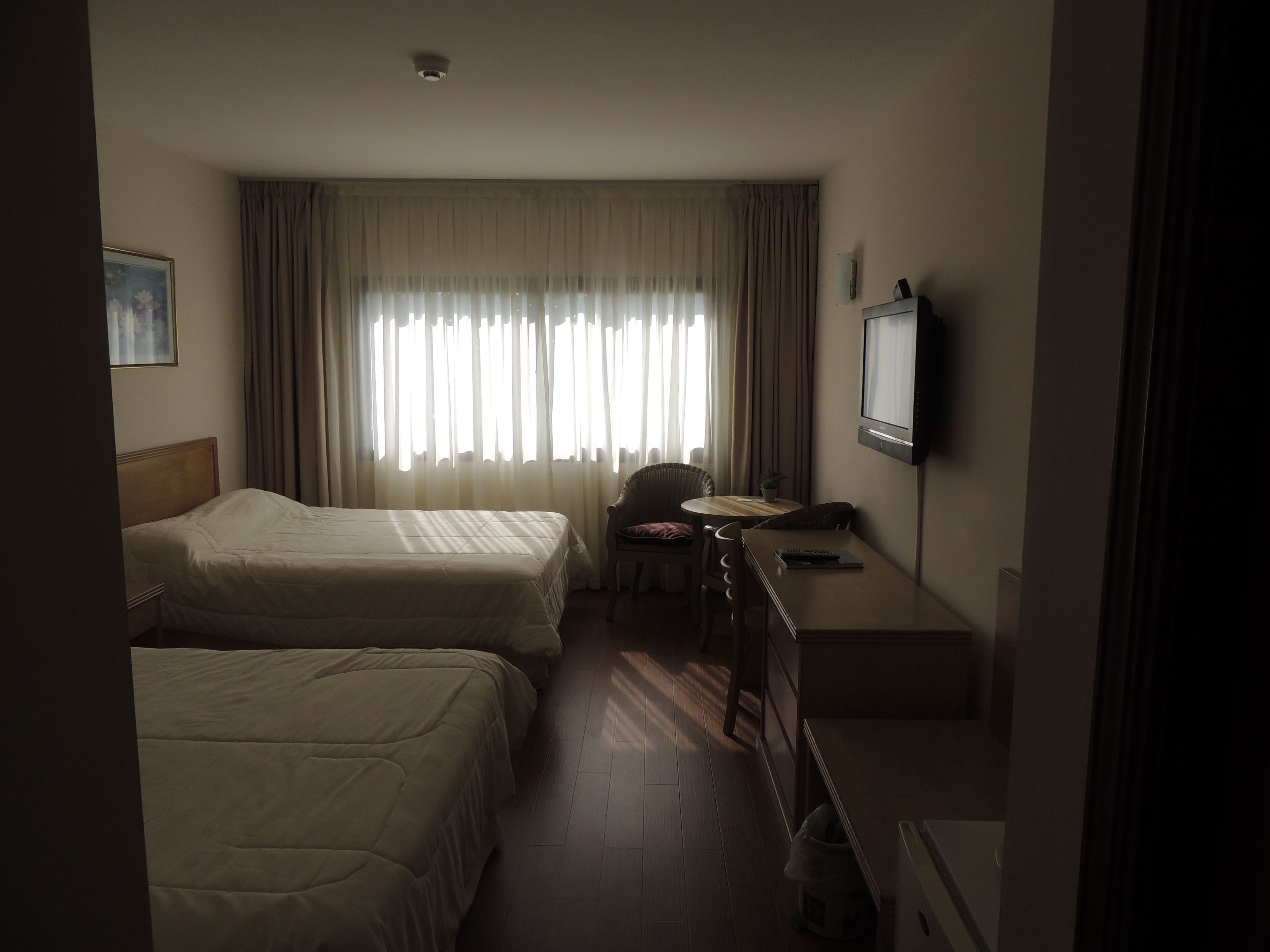 A hotel room with two beds, a desk, a chair, a television, and a window with curtains.