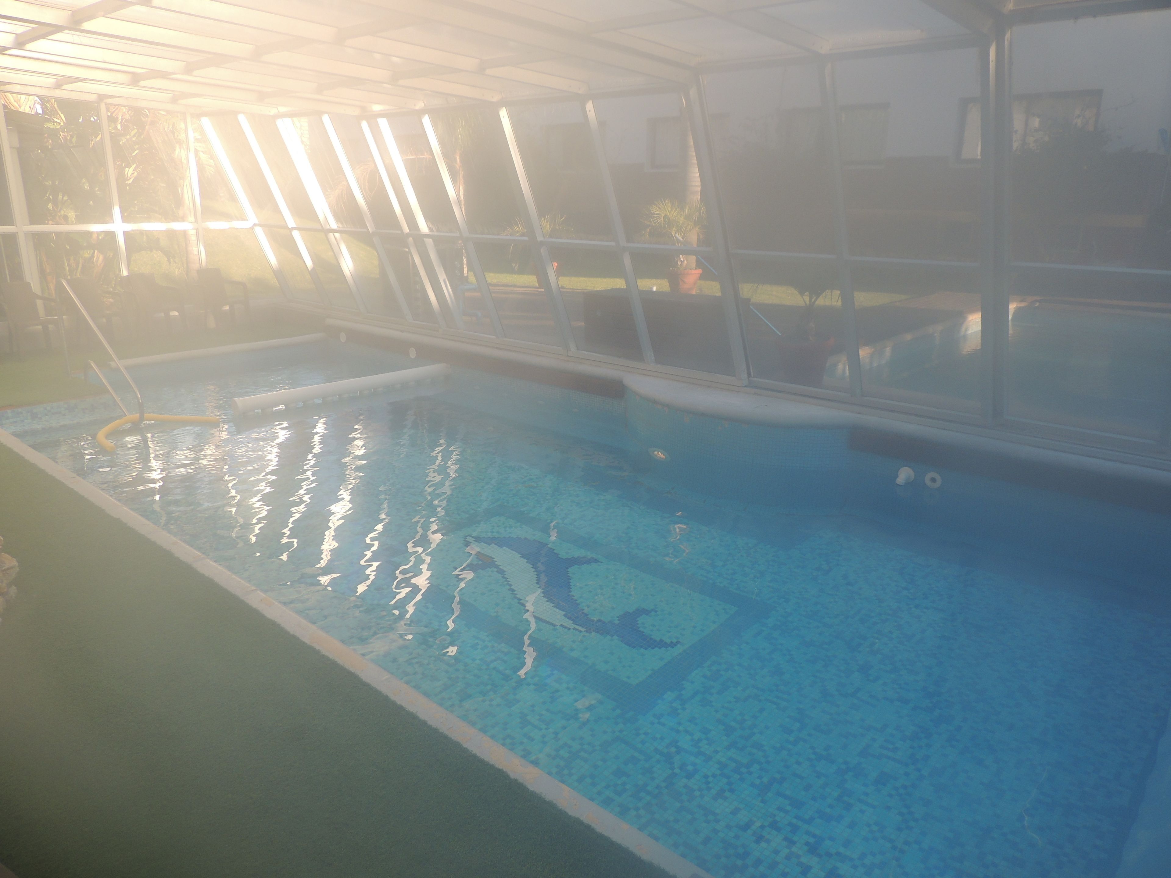 Une piscine intérieure à l’eau claire, entourée d’une paroi de verre et dotée d’un sol carrelé.