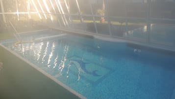 Una piscina interior con agua cristalina, rodeada por un recinto de vidrio y un suelo de baldosas.
