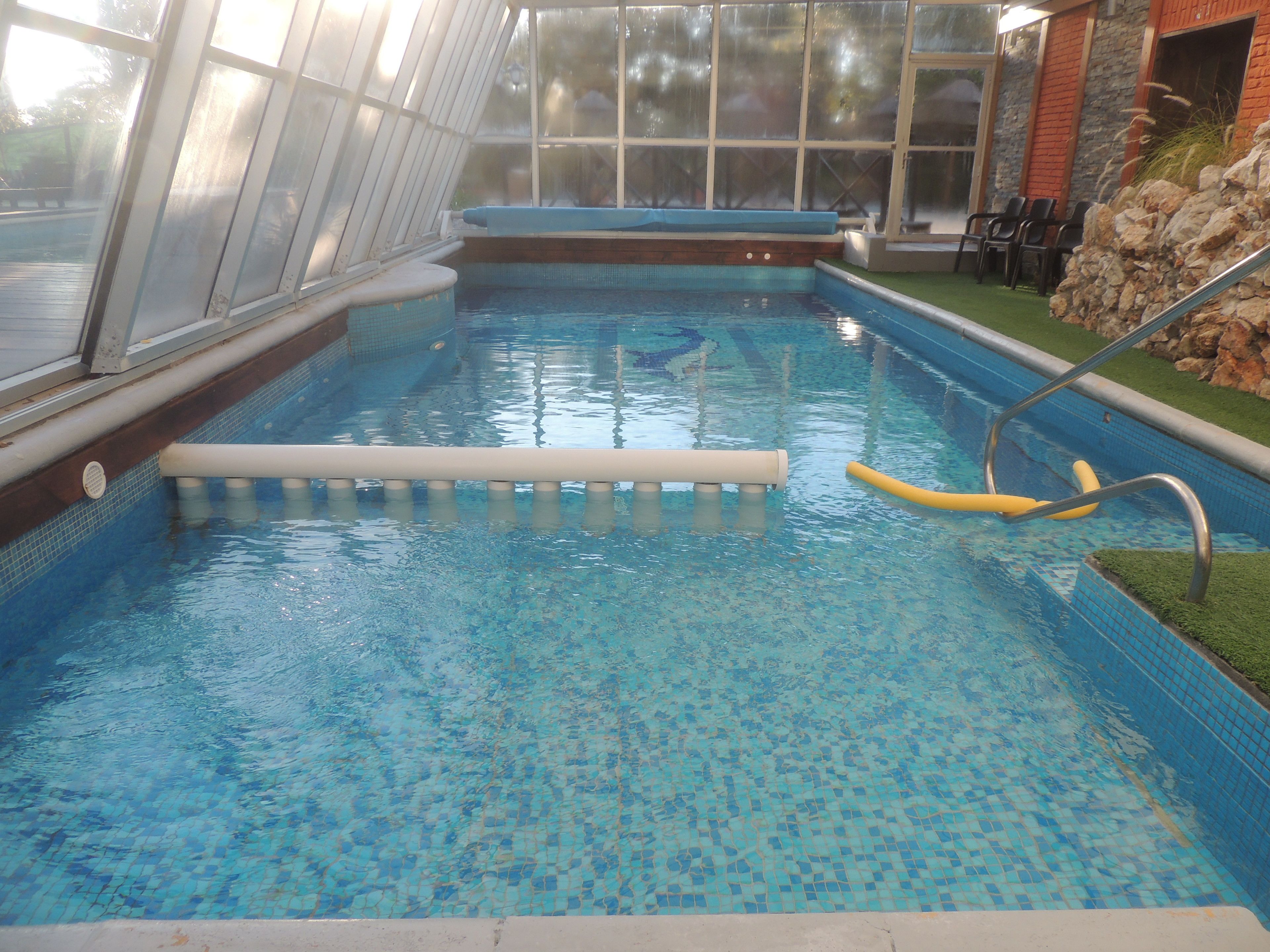 Una piscina interior con agua azul cristalina, un trampolín y una pared de piedra.