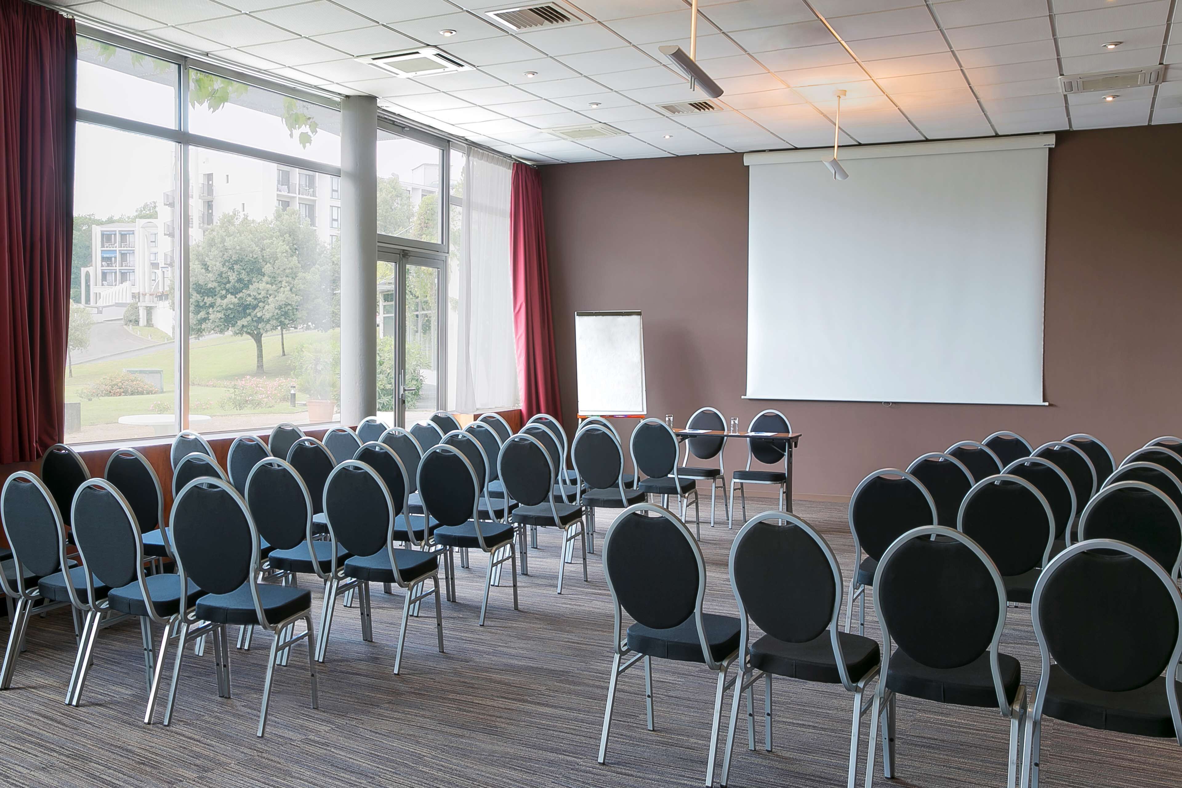 A conference room with rows of chairs, a projector screen, and large windows with curtains.