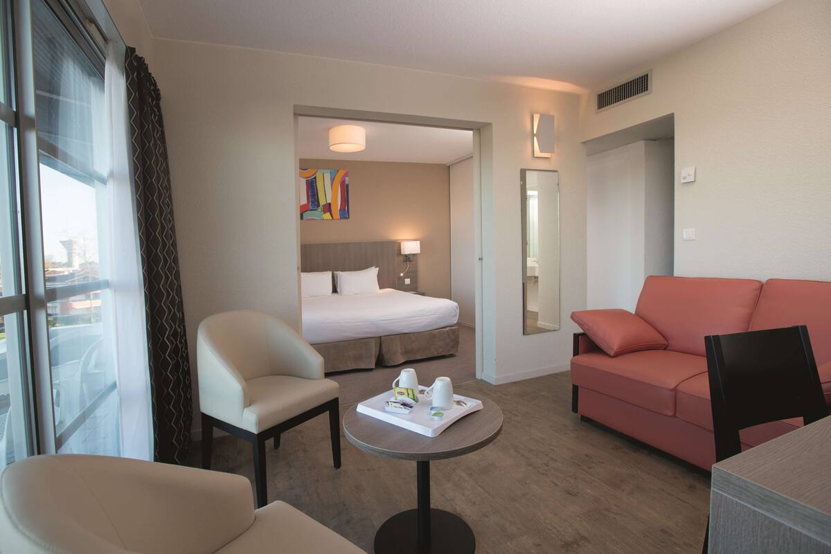 A hotel room with a bed, a sitting area with a table, a sofa, and a chair.